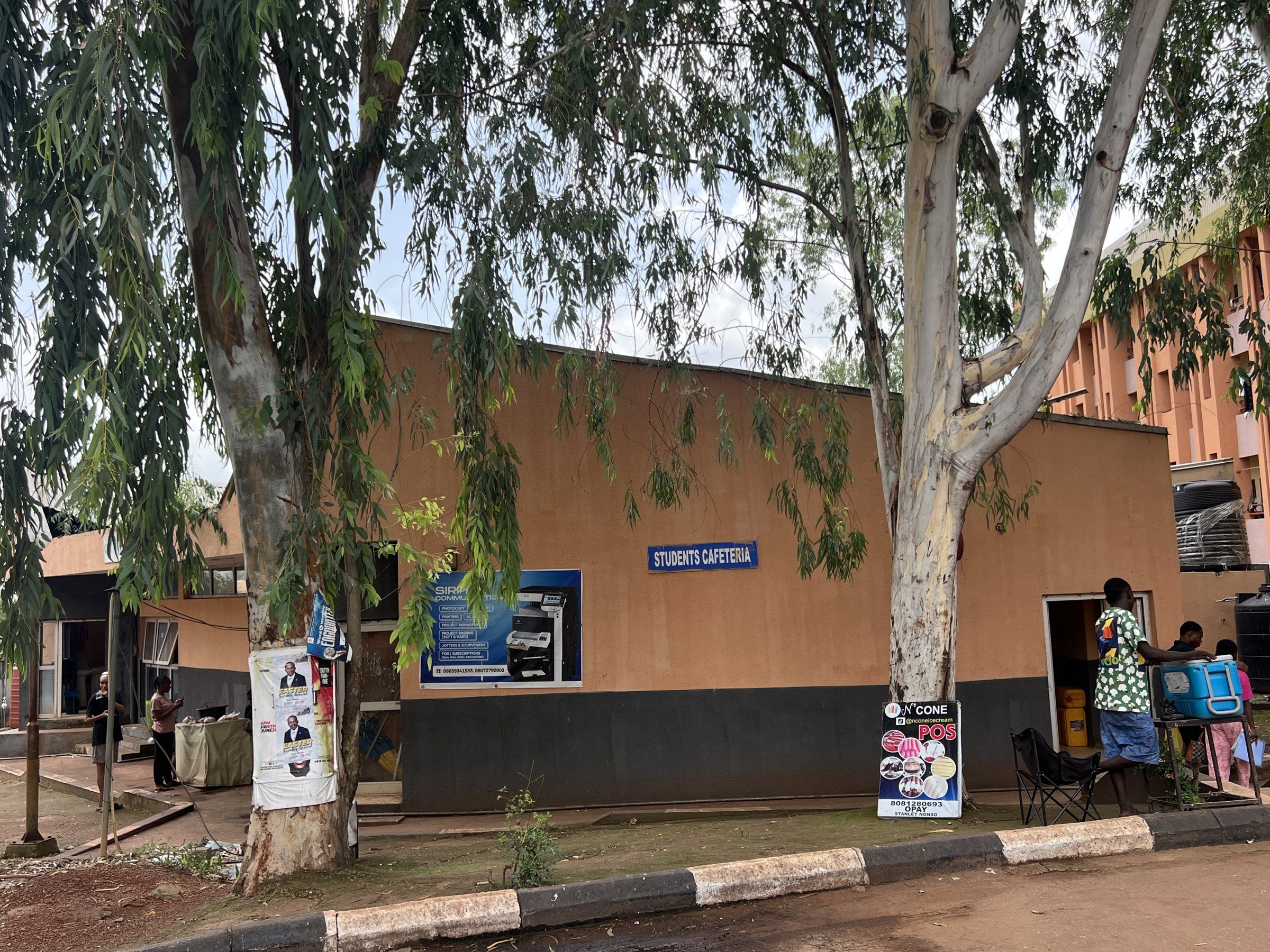 The students cafeteria, a single-storey building behind two tall trees.