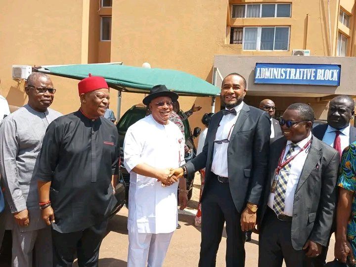 Two men shake hands outside the Administrative Block, with other officials standing beside them.
