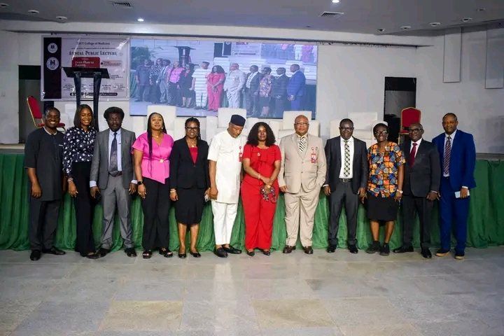 Thirteen guests standing in a row on a stage in front of a projector screen at the annual public lecture.