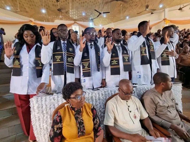 Graduating students in white coats and black sashes raise their right hands to take the oath.